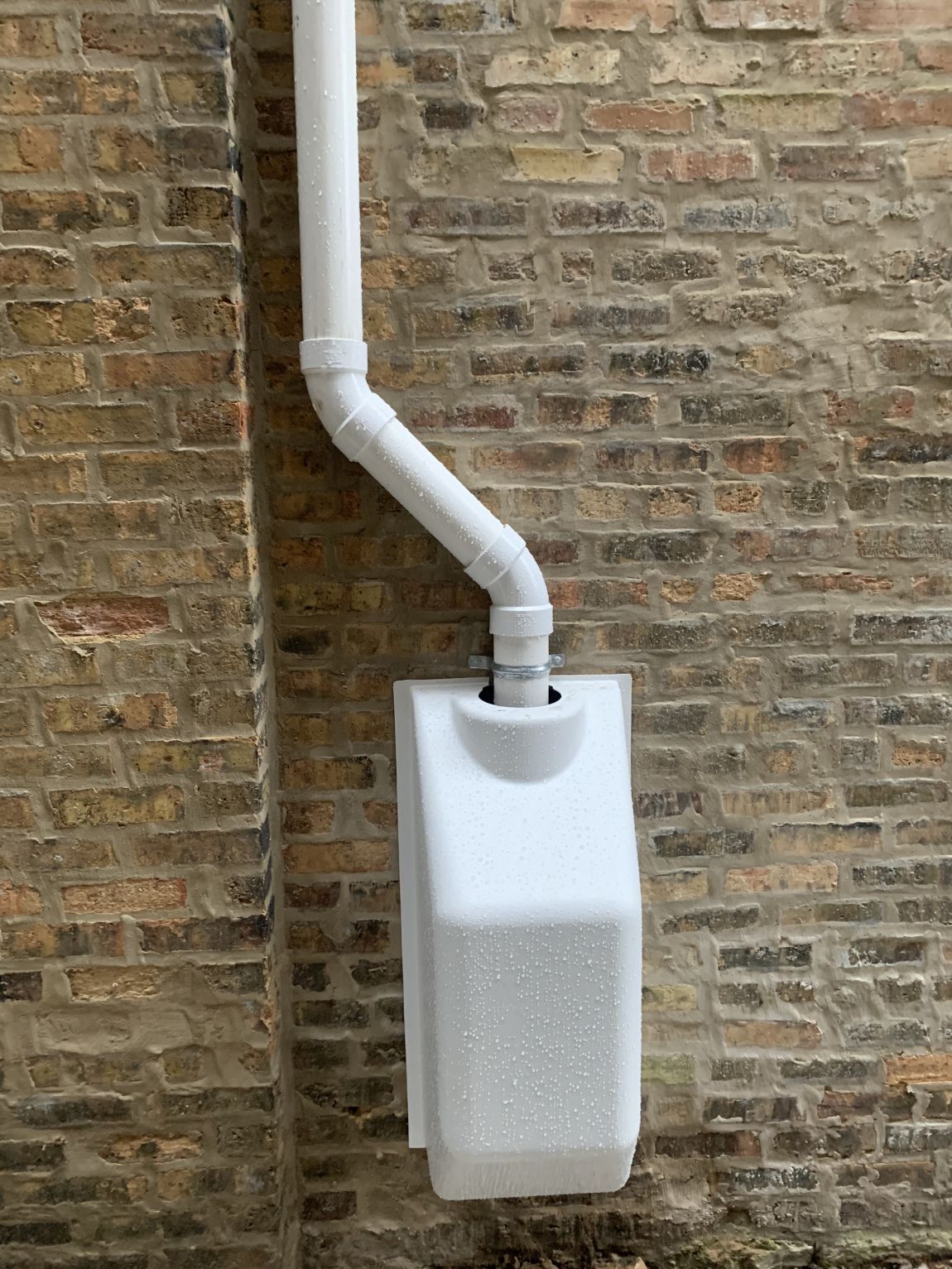 Exterior view of an installed active radon mitigation system in Aurora, featuring a sub-slab depressurization fan and PVC venting pipe mounted on a brick wall.